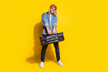 Photo of funny charming young guy dressed denim shirt smiling dancing holding boom box isolated yellow color background