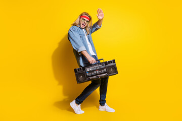 Photo of cool cute young gentleman wear jeans shirt dark glasses listening boombox waving arm smiling isolated yellow color background