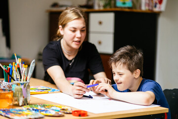 Close up of young female teacher sitting at desk with a Down syndrome schoolboy. Color painting on...