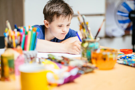 Disabled kids classroom, child with down syndrome having fun during study at school, schoolboy concentrate painting with hands in art classroom.