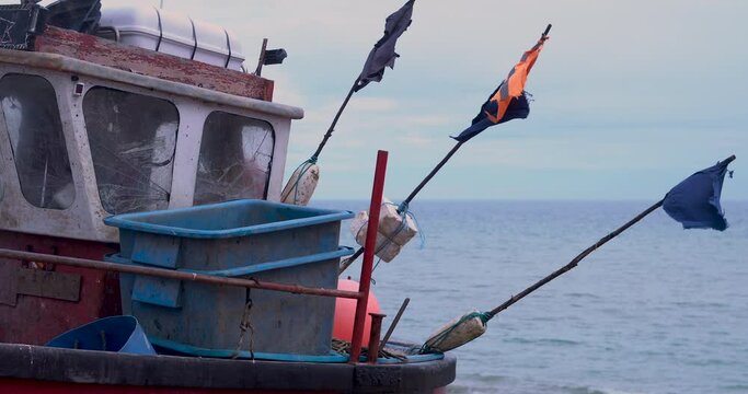 4K movie of a battered a fishing boat hauled onto the shingle beach at Hastings until the next high tide. The flags keep seagulls away from the decks and the window glass is shattered from high winds 