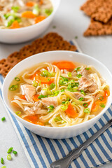 Noodle soup. Homemade soup with chicken broth, carrots and noodles in a bowl on a gray concrete background. Delicious autumn or winter soup.