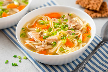 Noodle soup. Homemade soup with chicken broth, carrots and noodles in a bowl on a gray concrete background. Delicious autumn or winter soup.