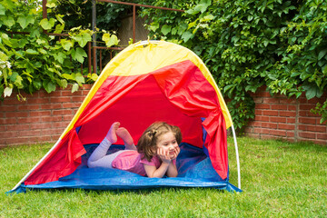 The little girl is playing and having fun in the shade of the tent in the garden of their house.