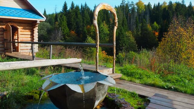 Holy spring with metal bowl and wooden house with plunge font pool for ablutions, gazebo for relaxing in a natural park..Nature park Stone Hill in the Mari El republik, Russia. Holy spring and font.
