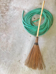 Broom and green hose on cement background 