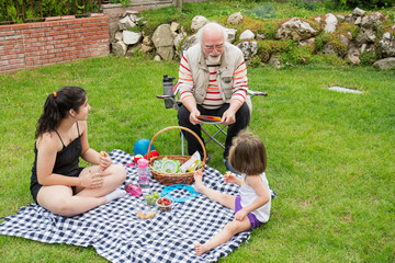 The girls are having a picnic with their grandparents. The old man is sitting on the chair.