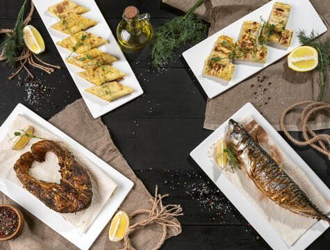 Grilled Salmon Steak, Baked Mackerel And Rolls Of Thin Flatbread On Black Table