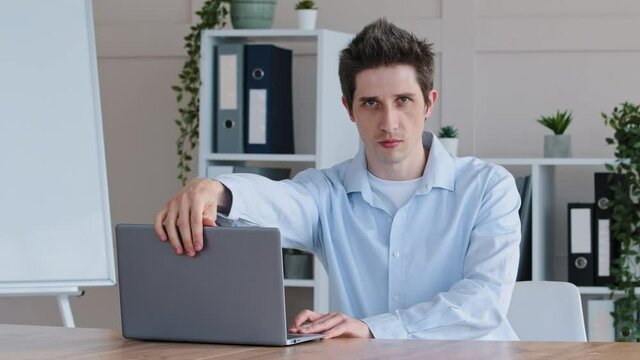 Funny comic caucasian freelancer business man doing mechanical movements with hands pretending to be robot takes laptop puts on office desk typing on keyboard points palm at computer looking at camera