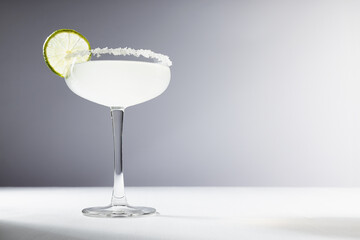 Bright margarita cocktail with sour green lime and sugar rim in elegant glass in sunlight on white...