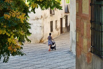 Obraz na płótnie Canvas Back view of a woman with a baby carriage walking down a narrow street in Granada (Spain)