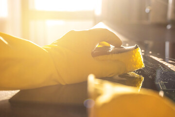Housework after work concept, hand in yellow glove with sponge, sunset, kitchen cleaning background photo