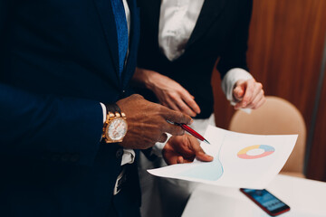 Businessman and businesswoman accountant team showing graph chart at office meeting. Business people group conference discussion sit at table with boss man and woman close up hands