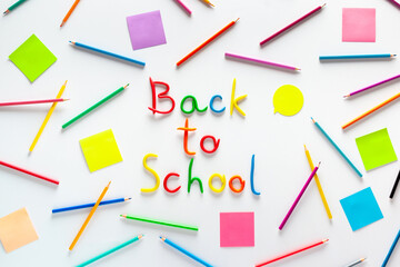 Plasticine inscription "Back to school", sticky notes and multicolored pencils on a white background. Pattern