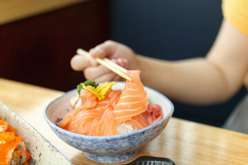 Asian woman eating salmon slice sashimi with rice in Japanese restaurant