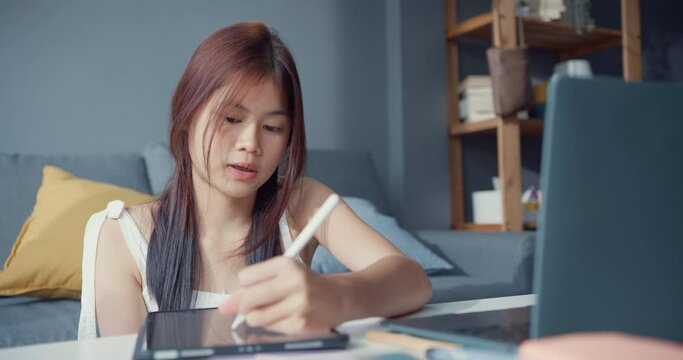 Young Asia girl teenager with casual use computer laptop focus to learn online write lecture in digital laptop in living room at home. Isolate education online e-learning coronavirus pandemic concept.