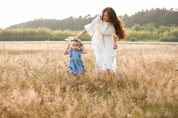 Naklejka na ściany i meble Young mother walking with her little daughter in the gold field. Family holiday in garden, park. Portrait mom with child together on nature. Mum, little daughter outdoors. Happy Mothers Day. Close up
