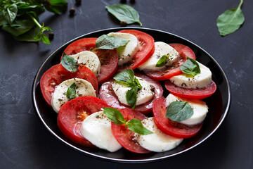 tomato salad with mozzarella and basil.Italian caprese salad with green and spice on the black plate with copy space. sliced red tomatoes, mozzarella cheese, green basil, olive oil on dark background