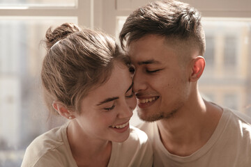 Family, closeness, relationship, feeling, tenderness concept. Pretty young couple smiling, hugging each other and posing at light room