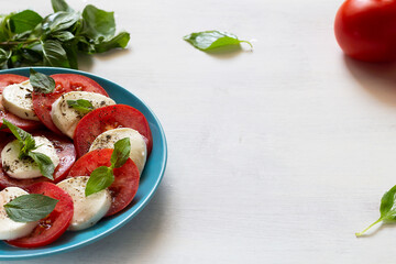 salad with tomato and basil.Italian caprese salad with fresh green on the blue plate. sliced red...