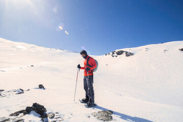 Fototapeta na wymiar A man standing in the mountain full of snow. holding hiking sticks. Winter trip. Red jacket
