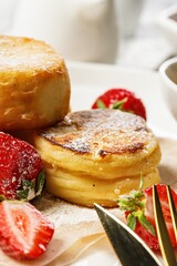 Close-up Cottage Cheese Pancakes with fresh strawberries and jam. Curd Cheese Pancakes on a white plate sprinkled with powdered sugar. Delicious homemade breakfast or snack on a wood background
