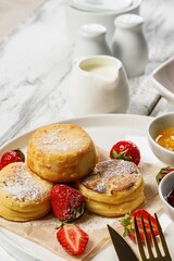 Vertical shot Cottage Cheese Pancakes with fresh strawberries and jam. Curd Cheese Pancakes on a white plate sprinkled with powdered sugar. Delicious homemade breakfast or snack on a wood background