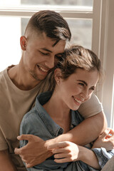 Happiness, love, feeling concept. Pretty young couple smiling, hugging each other and looking down in sunlit room