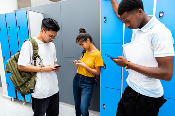 Group of multiracial teen students using their mobile phones in high school corridor.