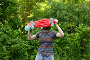 close up stylish girl carrying the penny board on the background of green trees