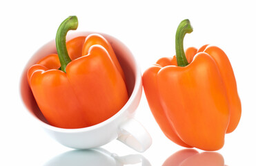 Two organic bell peppers with a white ceramic cup, close-up, isolated on white.