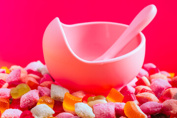 Children's tableware silicone bowl with spoon. Serving baby food, kid dishware.Pink silicone bowl and spoon are in a heap of sweets and marmalade. bright, colorful photo