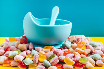 Children's tableware silicone bowl with spoon. Serving baby food, kid dishware.blue silicone bowl and spoon are in a heap of sweets and marmalade. bright, colorful photo