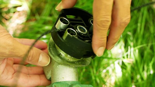 A man puts a knife on a lawnmower before cutting grass outside. Trimmer in the hands of a man, assembly and cleaning. A close-up of a garden tool.