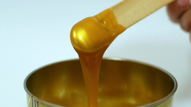 Gold depilatory wax drips from the wooden skewer before the procedure. Beauty and cosmetology removal of unwanted hair with a natural remedy.