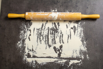 Background of flour scattered on a dark table and a rolling pin for dough. Background with place for text. Baking, bread
