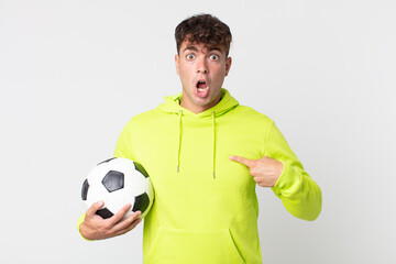young handsome man looking shocked and surprised with mouth wide open, pointing to self and holding...