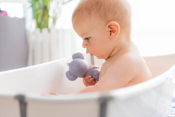 Caucasian boy playing with a toy in a portable bathtub. Concept of home games in the water. Horizontal plane with side view.