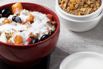 Portion of healthy fruits salad covered with granola, quinoa and yogurt in a red bowl.