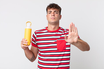 young handsome man looking serious showing open palm making stop gesture and holding a coffee...