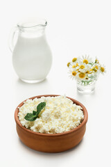 Cottage cheese granulated in earthenware next to a jug of milk. Close-up, selective focus, bright white background. Soft cottage cheese, natural healthy food, complete diet food
