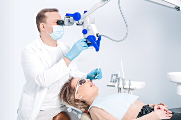 Naklejka na ściany i meble Pretty caucasian woman in dentist chair in modern dental clinic. Doctor checkup the patient using dental professional equipment, microscope. Female patient receiving dental care.