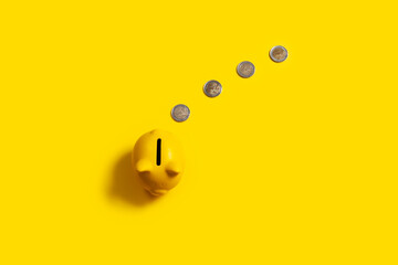 top view of piggy bank with coins on yellow background