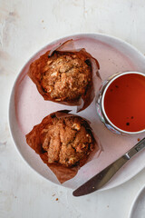 Two muffin with walnuts on a pink plate with a knife and a cup of tea. Light background. 