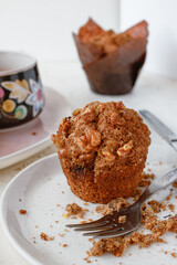 Two muffin with walnuts on a white plate with a fork. and a cup of tea. Light background. 