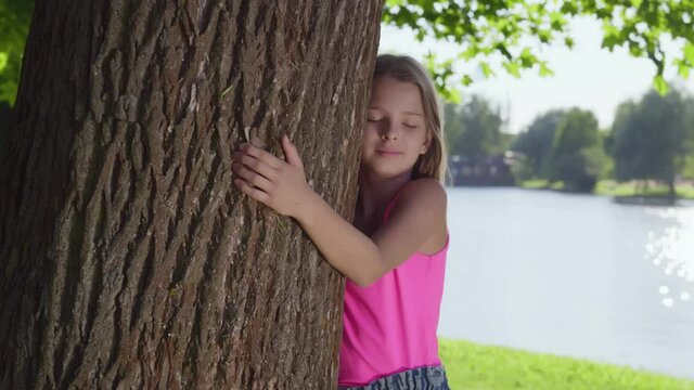 Smiling teenage girl hugging tree with eyes closed at park