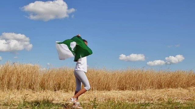 Girl waving flag of Pakistan outdoors over blue cloudy sky and golden wheat. Happy independence day of Pakistan.