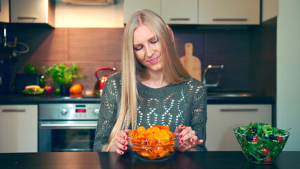Young lady preferring crisp to salad. Attractive young woman choosing to eat healthy crisp for breakfast while sitting at table in stylish kitchen.