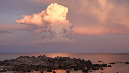 Huge masses of clouds hanging in red and white and crimson hues in the sky and crimson cliffs and pebbles on the beach