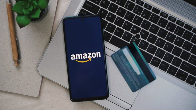 Dobrich, Bulgaria – 2021, July, 21: Mobile phone with Amazon logo. Laptop and credit card as background. Worldwide purchasing products. Editorial illustrative image for online shopping at Amazon.com
